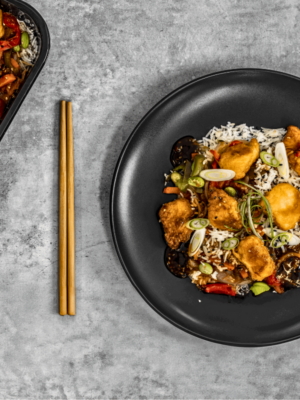 Un plat de poulet Général Tao servi dans une assiette blanche, accompagné de riz blanc parfumé et de légumes colorés, le tout nappé d'une sauce brune brillante. Vendu par AppétitGo, prêt à être livré et dégusté.