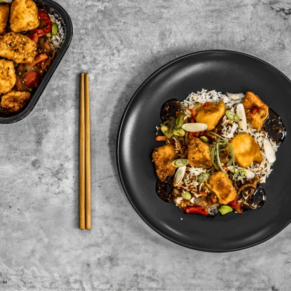 Un plat de poulet Général Tao servi dans une assiette blanche, accompagné de riz blanc parfumé et de légumes colorés, le tout nappé d'une sauce brune brillante. Vendu par AppétitGo, prêt à être livré et dégusté.