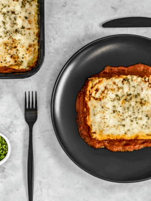 Une assiette de lasagne savoureuse, avec des couches de pâtes dorées, une riche sauce à la viande et du fromage fondant, garnie de basilic frais. Un plat appétissant prêt à être dégusté.