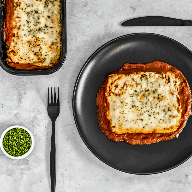 Une assiette de lasagne savoureuse, avec des couches de pâtes dorées, une riche sauce à la viande et du fromage fondant, garnie de basilic frais. Un plat appétissant prêt à être dégusté.