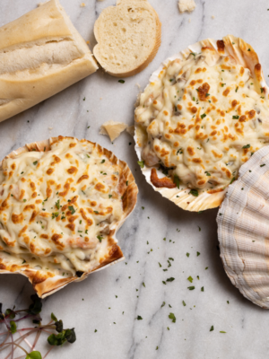 Deux coquilles de crevettes crémeuses à l'ail, délicatement présentées sur une table en marbre, accompagnées d'une baguette de pain croustillante, prête à être dégustée.