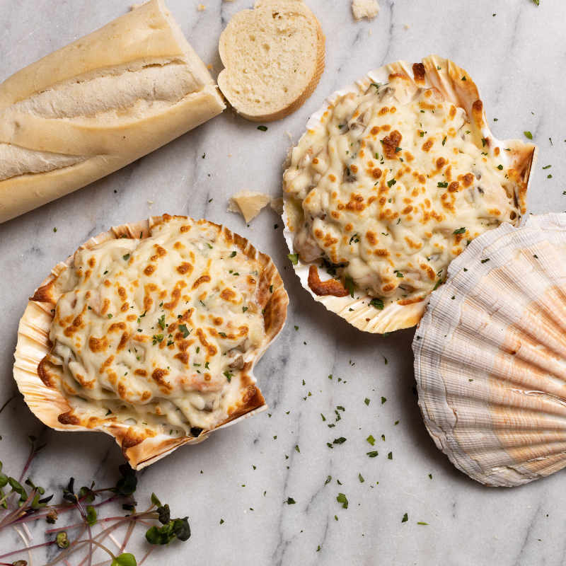 Deux coquilles de crevettes crémeuses à l'ail, délicatement présentées sur une table en marbre, accompagnées d'une baguette de pain croustillante, prête à être dégustée.