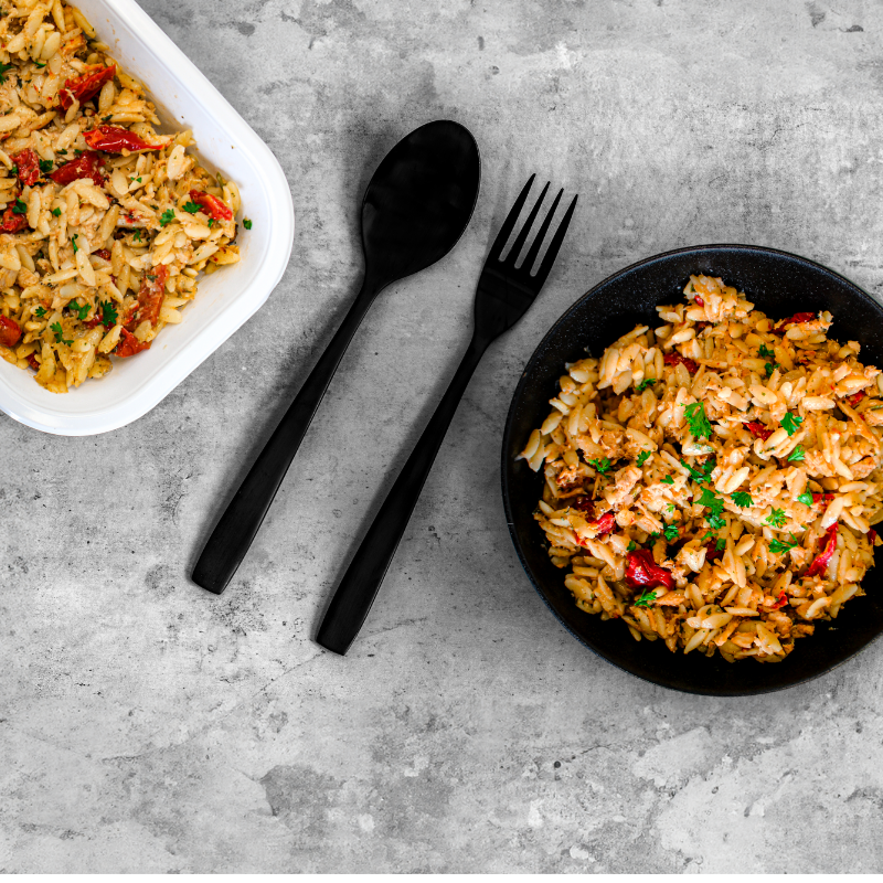 Image d'orzo crémeux au poulet et tomates séchées présenté dans une assiette et un contenant de repas rapide. Prêt à être cuisiné et dégusté.